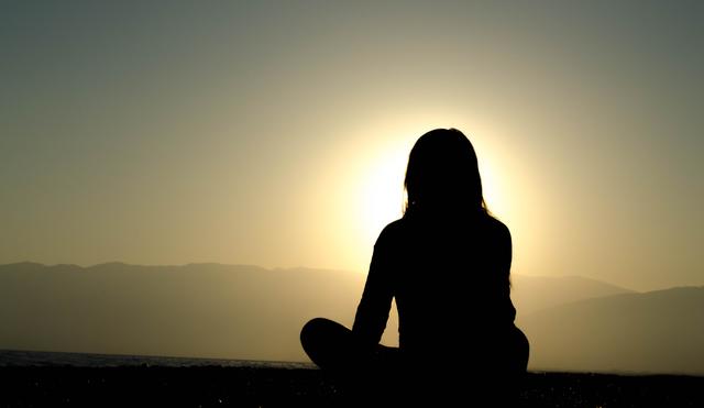 Silhouette of a woman meditating on the beach at sunset.